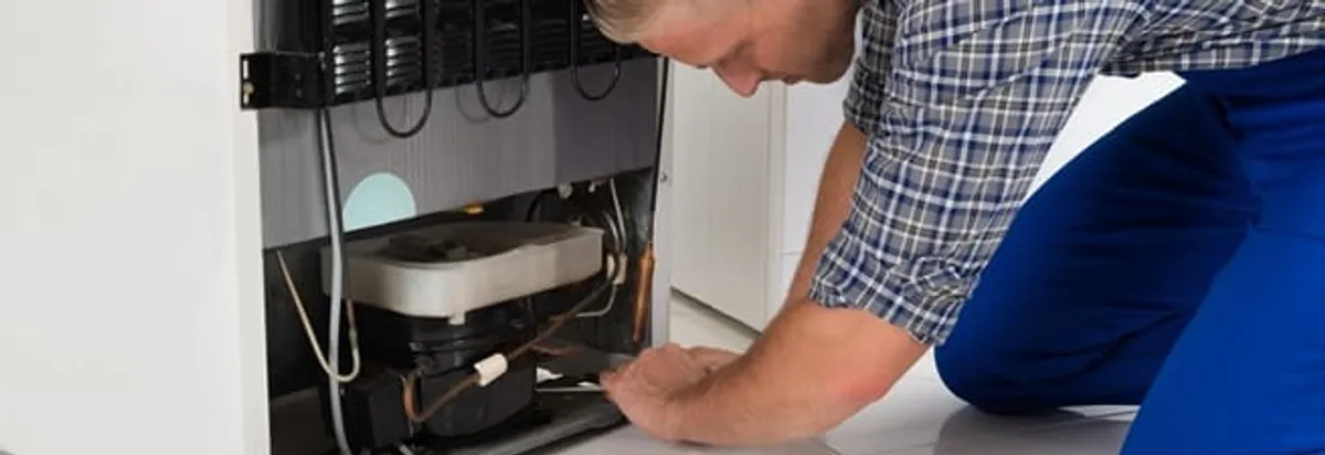 Refrigerator repair technician servicing the compressor and condenser area in Lakeland, FL